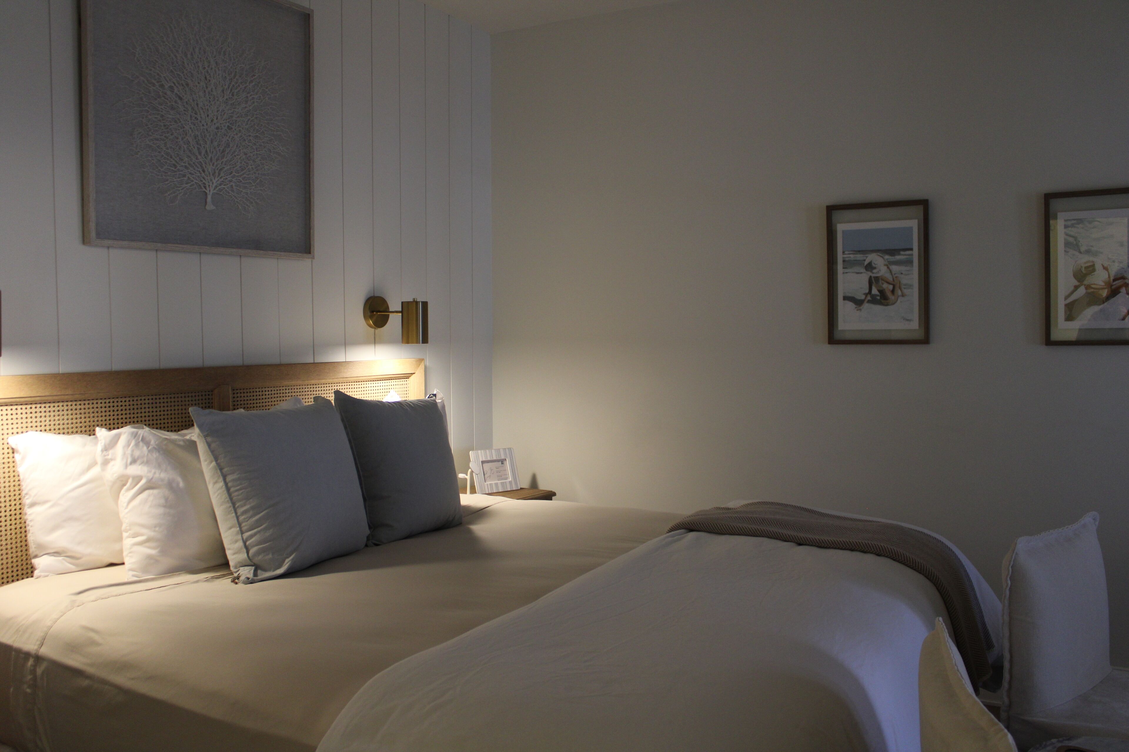 A hotel room with a large bed, a nightstand, a wall-mounted lamp, and framed artwork.