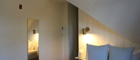 A hotel room with a bed, a bedside table, a nightstand, a mirror, and a wall-mounted light fixture.