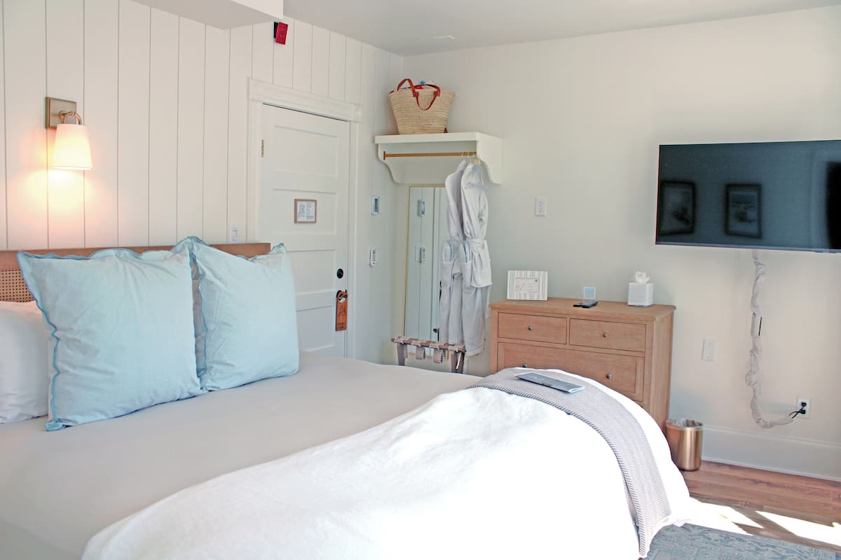A bedroom with a bed, a dresser, a mirror, a robe rack, and a television.