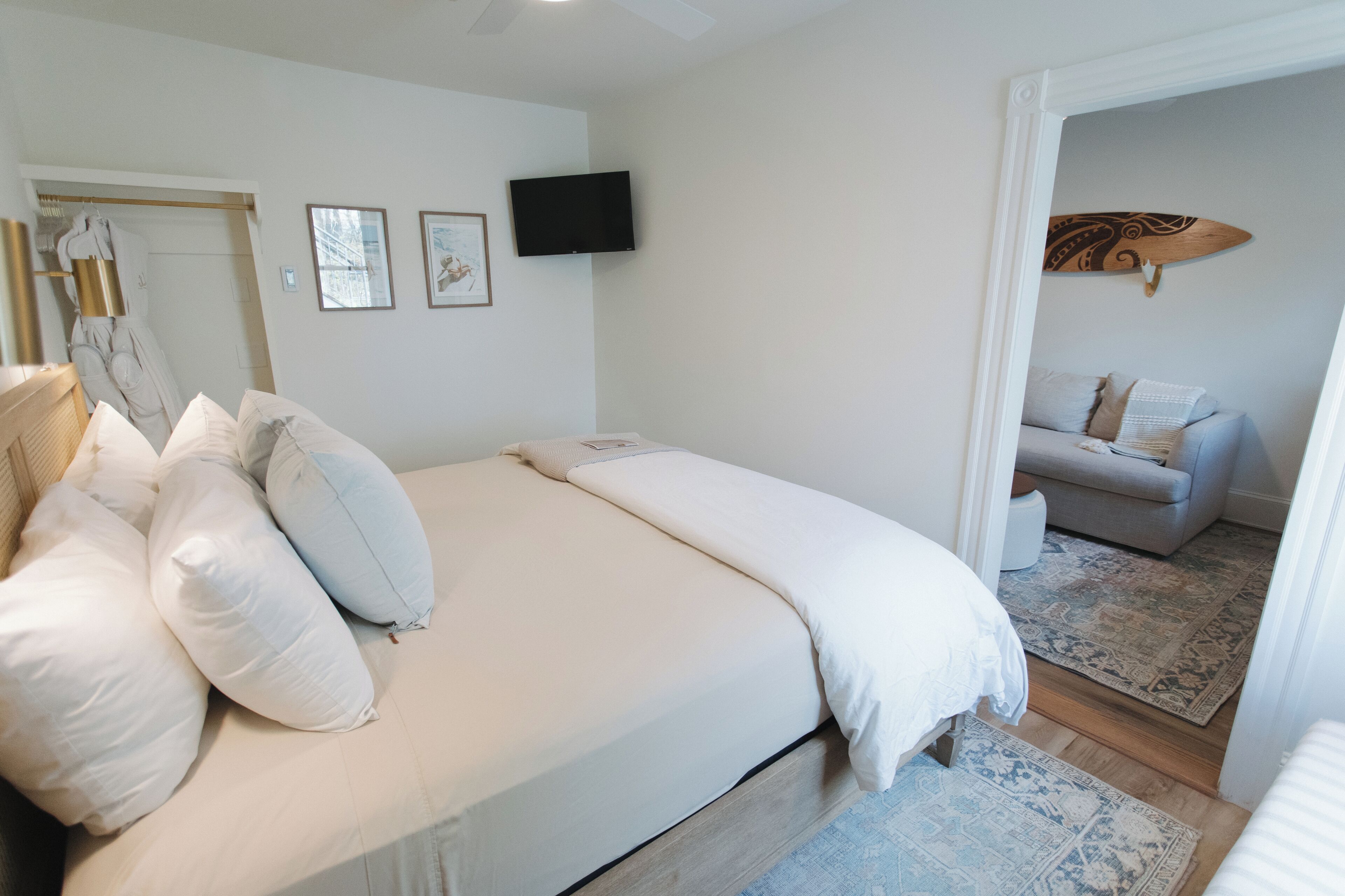 A bedroom with a large bed, a television on the wall, and a view into an adjacent living area.