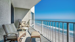En balkon med udsigt over havet, møbleret med stole og en bænk.