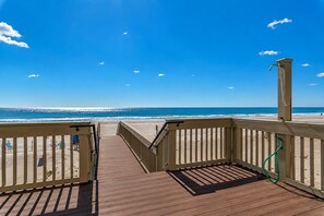 A wooden deck leading to a beach with a clear view of the ocean and a single chair on the sand.
