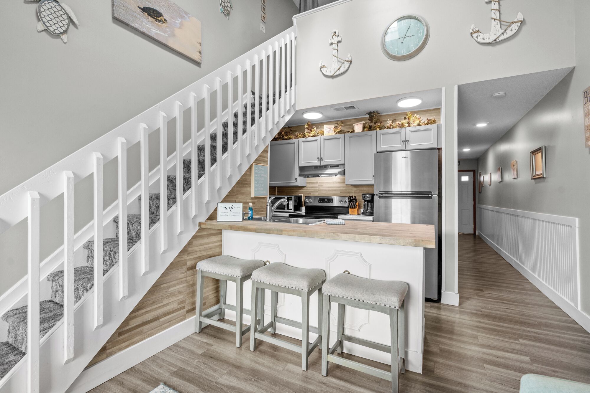 A modern kitchen with a central island, stainless steel appliances, and a white staircase.
