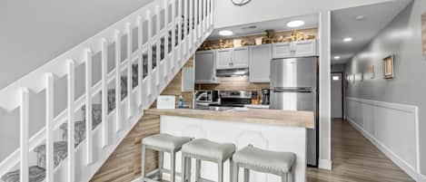 A modern kitchen with a central island, stainless steel appliances, and a white staircase.