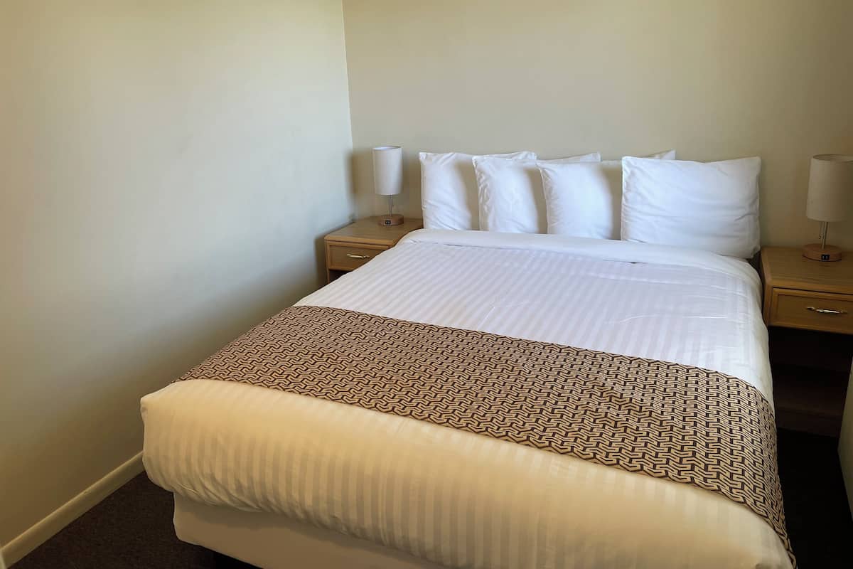 A neatly made bed with a patterned throw, two bedside tables with lamps, and a plain wall.