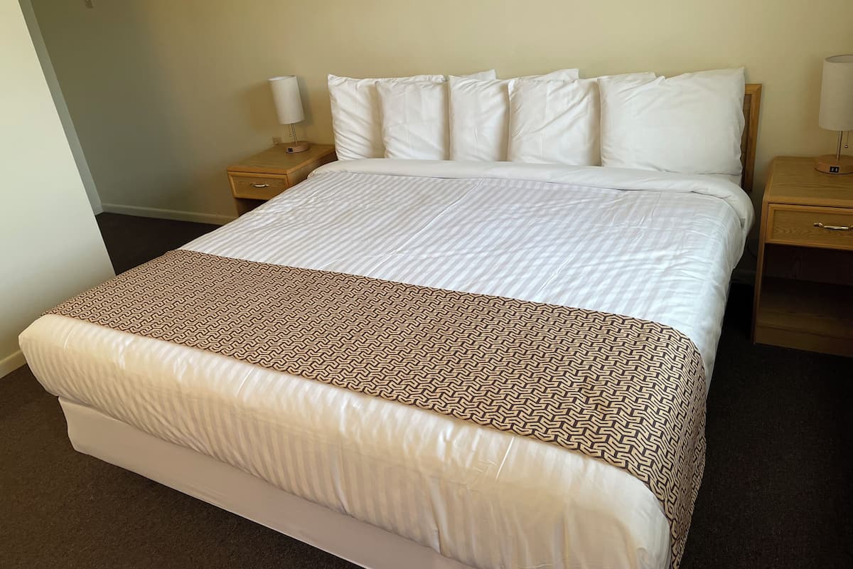 A neatly made bed with a patterned throw, two bedside tables with lamps, and a plain wall.