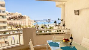 Un balcon avec une table et des chaises, une bouteille de vin et un panier de fruits.