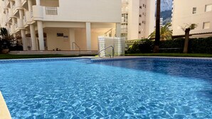 Une piscine à l’eau d’un bleu cristallin, entourée d’un bâtiment blanc doté de balcons et d’un espace abrité.