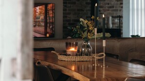 Ett matbord i trä med ljus, en vas i glas med blommor och en vävd bordsduk.