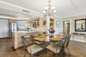 A modern kitchen with a central island, wooden cabinets, and a dining area with metal chairs and a glass table.