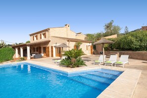 Une piscine avec des chaises longues, un espace patio et un bâtiment à la façade en pierre.