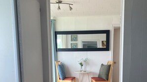 A doorway leading to a room with a wooden floor, two chairs, a small table, and a mirror on the wall. - Ocean view! Relax at this peaceful getaway only steps from the beach! (Grand Beach)