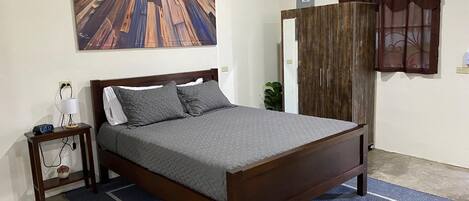 Une chambre à coucher avec un lit en bois, une table de chevet avec une lampe, un tableau accroché au mur et une fenêtre avec des rideaux.