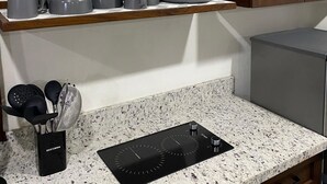 A kitchen with a granite countertop, a black induction cooktop, a coffee maker, and a small potted plant on a wooden shelf. - Tres Cielos Cabanas (Playa Las Hojas)