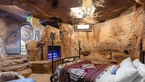 A cave-like room with a bed, a fireplace, and a chandelier.