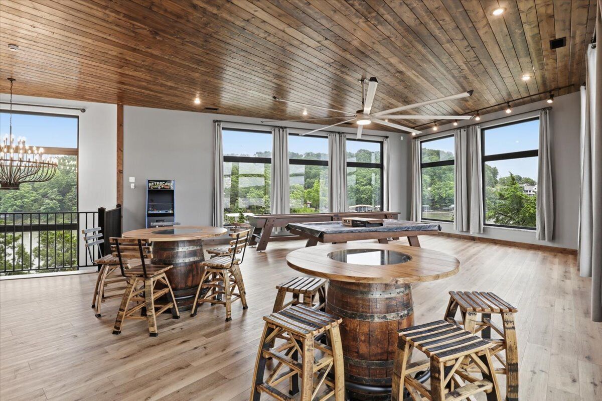 A spacious room with a wooden ceiling, large windows, a round wooden table, and rustic wooden stools.