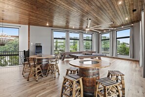 Une pièce spacieuse avec un plafond en bois, de grandes fenêtres, une table ronde en bois et des tabourets rustiques en bois.