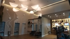 Un hall d’hôtel moderne comprenant un comptoir d’accueil, un espace salon et un écran de télévision diffusant un programme.