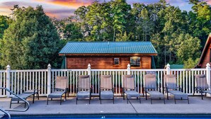 A wooden cabin with a blue roof, surrounded by a white picket fence, and a pool area with lounge chairs. - Blackberry Bliss: Pet Friendly, Free Attraction Tixs, Hot Tub, Pool Access, in Pigeon Forge (Pigeon Forge)