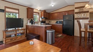 Eine kleine Küche mit Holzschränken, einer zentralen Kücheninsel, einem Kühlschrank, einer Mikrowelle und einem Fernseher.