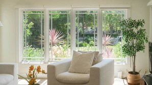 Una sala de estar con un sofá color crema, una mesita de centro con una revista, una planta en maceta y un mueble para televisor.