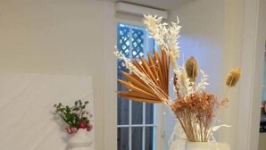 Una mesa de comedor con mantel blanco, dos jarrones con plantas secas y una ventana con vistas.