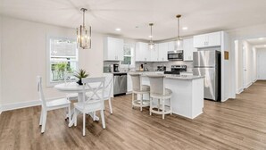 Una cocina moderna con armarios blancos, una isla central con taburetes e iluminación colgante.