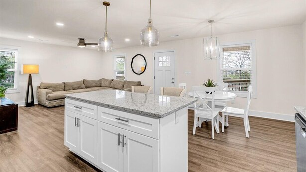 Una cocina moderna con armarios blancos, una isla con encimera de granito e iluminación colgante.
