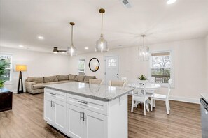 Una cocina moderna con armarios blancos, una isla con encimera de granito e iluminación colgante.