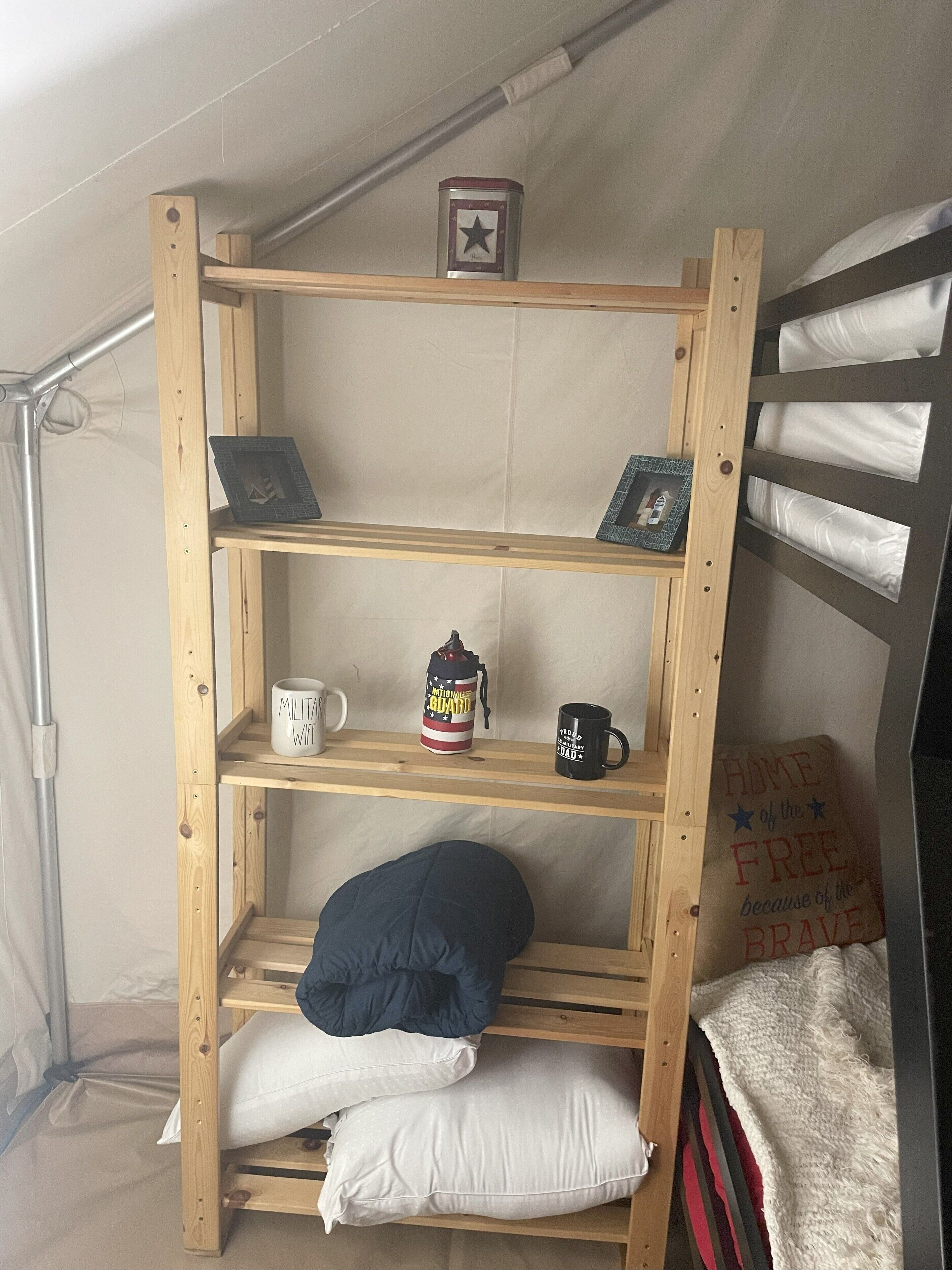 Een stapelbed met een plank erboven, waarop een mok, een waterfles en een ingelijst fotol staan.
