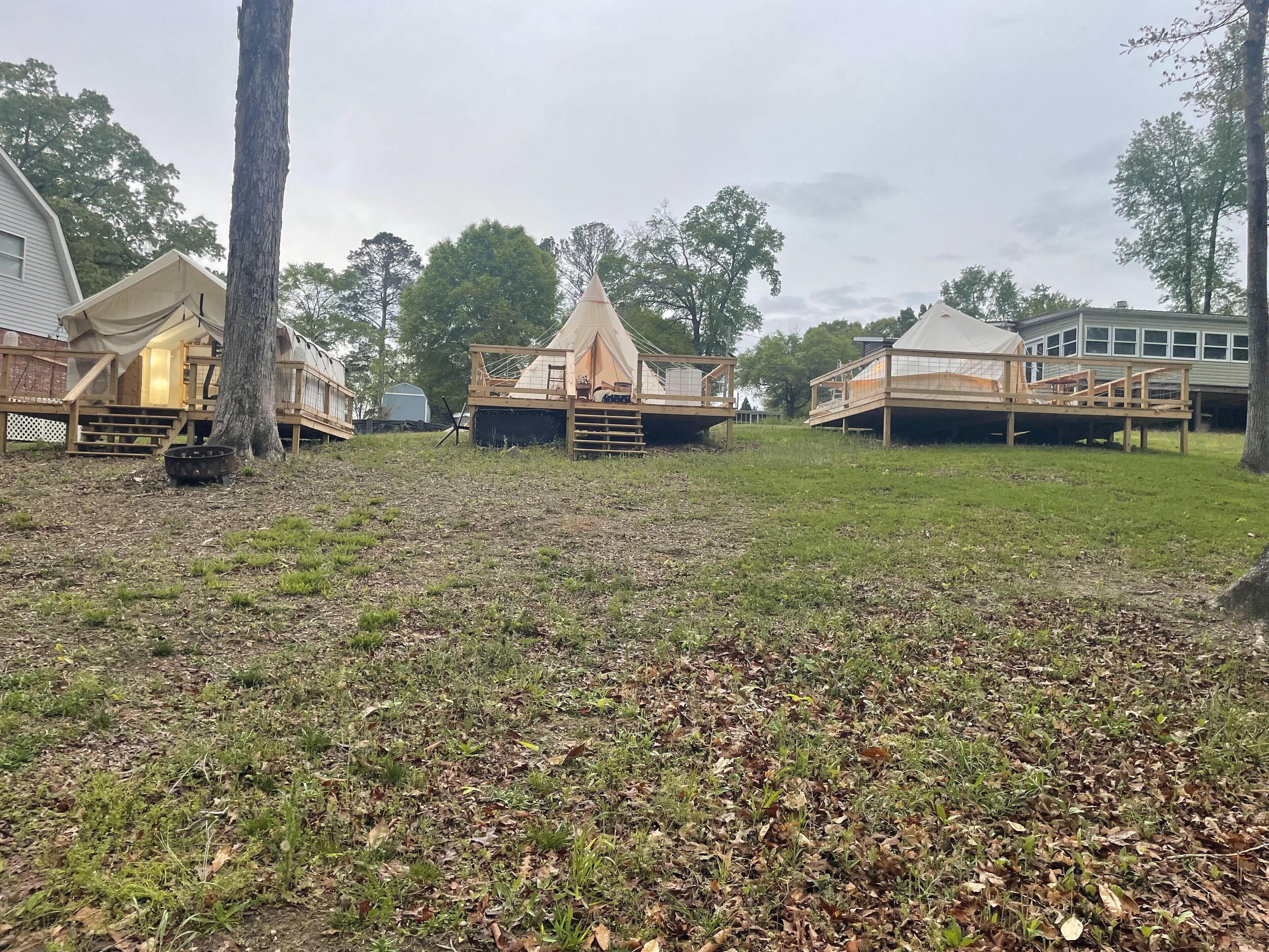 A campsite with several wooden tents and cabins, surrounded by trees and grassy areas.