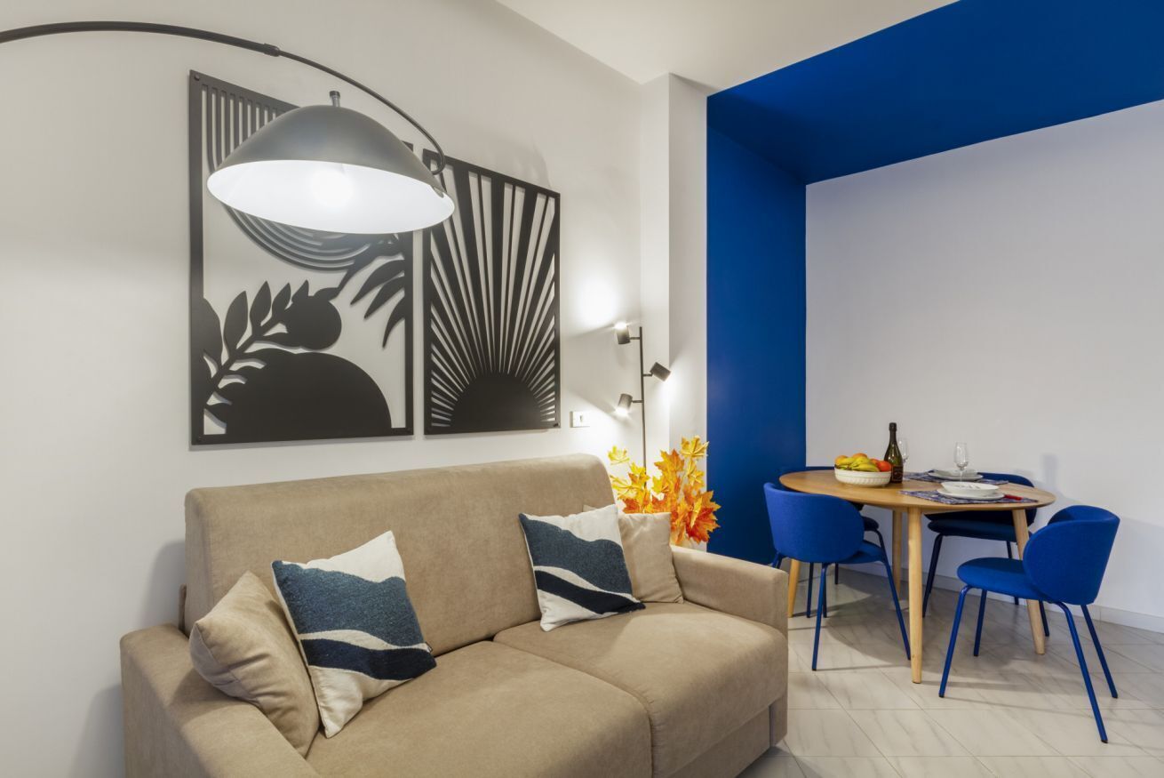 Un salon moderne avec un canapé, une table à manger et des chaises, ainsi qu’une lampe fixée au mur.