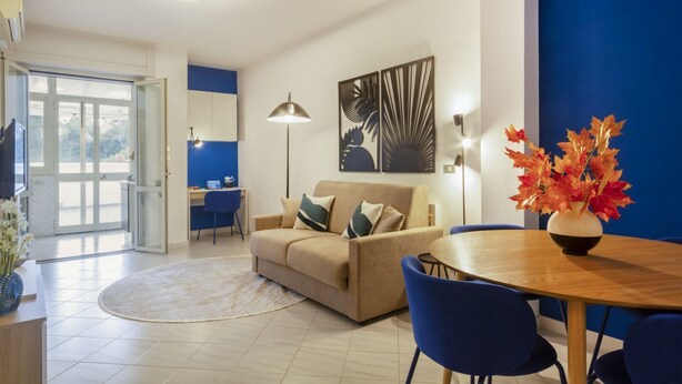 Ein modernes Wohnzimmer mit einer Couch, einem Esstisch, Stühlen, einer Lampe und Kunstwerken an der Wand.
