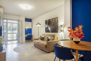 A modern living room with a sofa, a dining table, chairs, a lamp, and artwork on the wall.