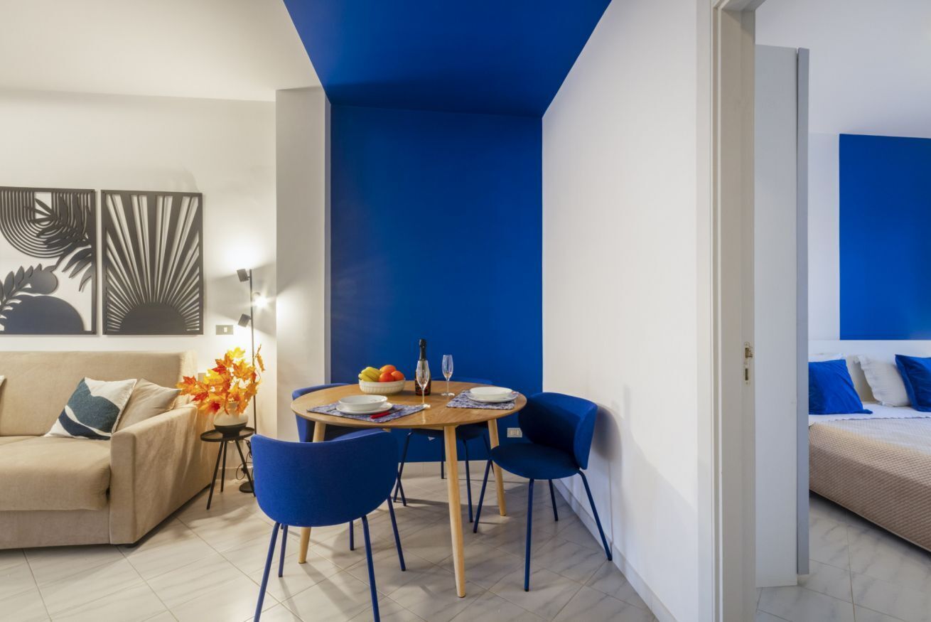 Un salon moderne avec un mur d’accent bleu, une table à manger ronde avec des chaises, un canapé et un lit agrémenté de coussins bleus.