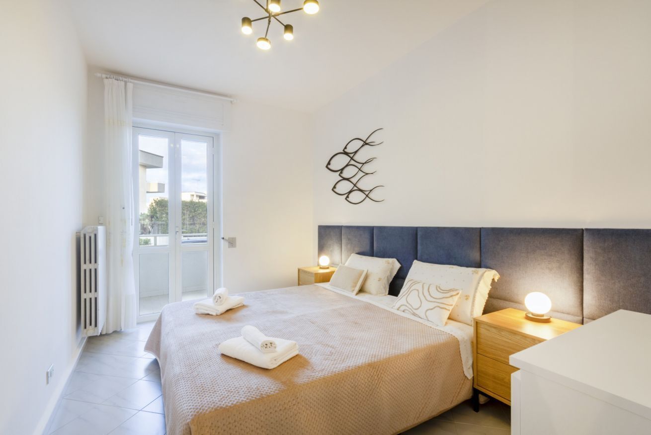 Une chambre à coucher comprenant un lit, des tables de chevet, un radiateur, une fenêtre et un luminaire fixé au mur.