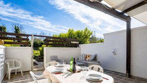 Eine Terrasse mit einem runden Esstisch, umgeben von weißen Stühlen, unter einer Pergola.