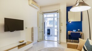 Ein modernes Wohnzimmer mit Flachbildfernseher, Essbereich mit Tisch und Stühlen, einer Couch und einer Lampe.