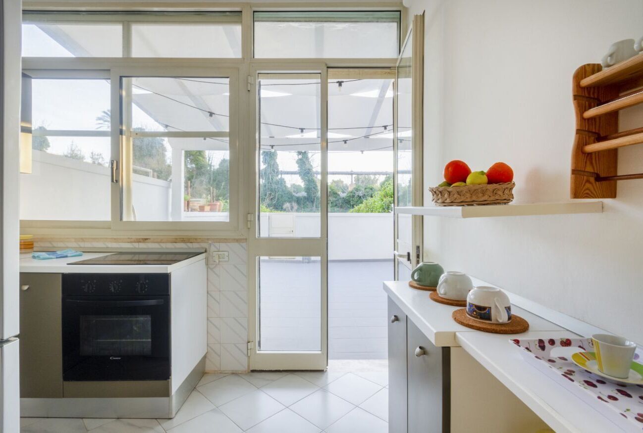 Une cuisine équipée d’un four encastré, un coin repas avec une table et des chaises, et une vue à travers une porte vitrée.