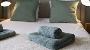 A neatly made bed with green pillows and folded towels.