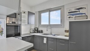 A modern kitchen with grey cabinets, a stainless steel microwave, an oven, a sink, and a window above the countertop.