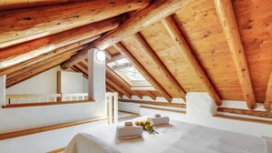 Une pièce aux hauts plafonds, avec des poutres en bois, une lucarne et un lit soigneusement fait, agrémenté de serviettes et de fleurs.