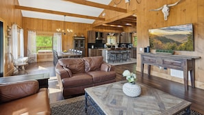 A spacious living room with a brown leather sofa, a wooden coffee table, and a dining area with a chandelier.