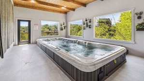A spa area with a hot tub, large windows, and a view of greenery.