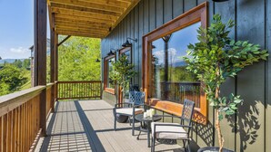 A wooden deck with outdoor seating, potted plants, and large windows.