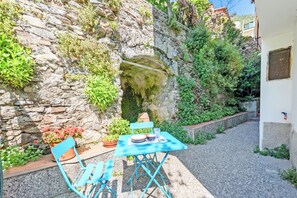 A stone wall with a cave-like opening, a blue metal table with chairs, and potted plants. - Yard Apartment with Balcony in Vernazza, Vernazza, Italy (Vernazza)