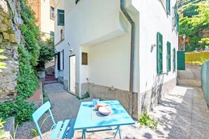 Un patio con una mesa y sillas, un muro de piedra y un edificio con contraventanas verdes.