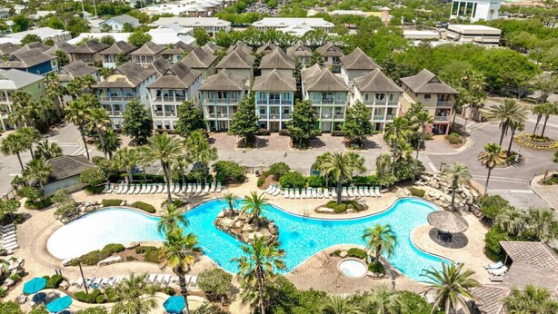 Een resort met een centraal gelegen zwembad, meerdere gebouwen en weelderige beplanting.