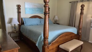 Un lit à baldaquin avec une structure en bois, un banc au pied du lit, deux tables de chevet avec des lampes et un tableau au mur.
