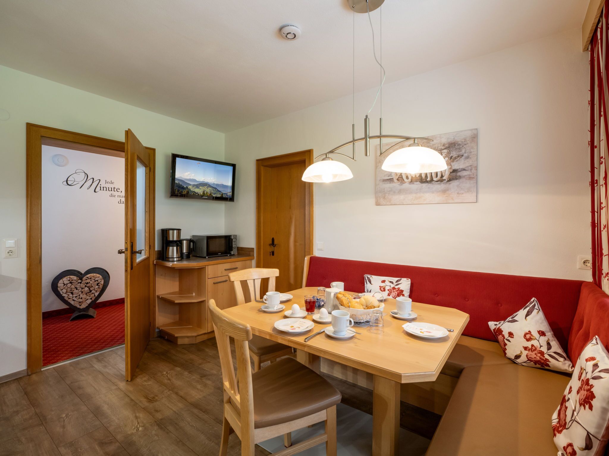 A cozy dining area with a wooden table set for breakfast, a red sofa, and a television on the wall.